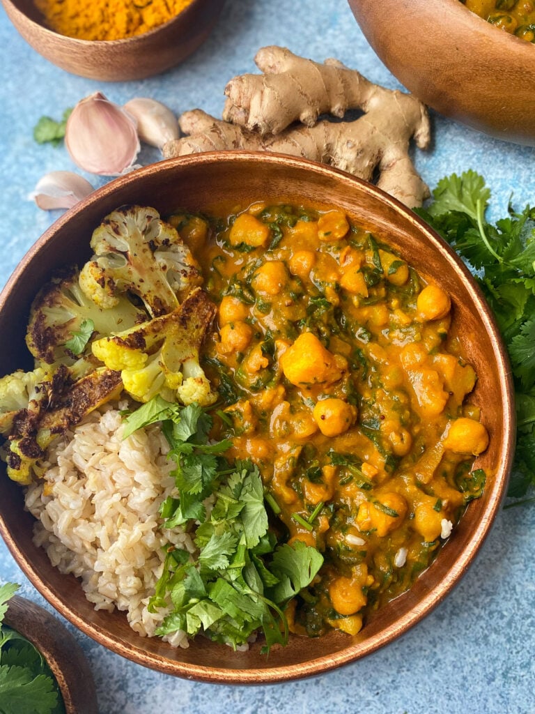 homemade chana saag aloo with Curry Chickpeas, Greens and Potatoes in a brown bowl by fresh cilantro and ginger.