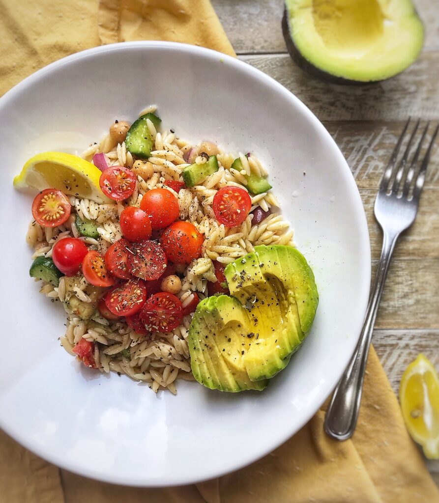 overhead view of a refreshing greek inspired orzo salad with cherry tomatoes, cucumber, red onion, and avocado.