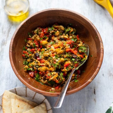 Overhead view of a bowl of eggplant salad, a side of pita bread and some extra virgin olive oil