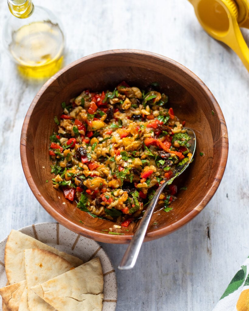 Overhead view of a bowl of eggplant salad, a side of pita bread and some extra virgin olive oil
