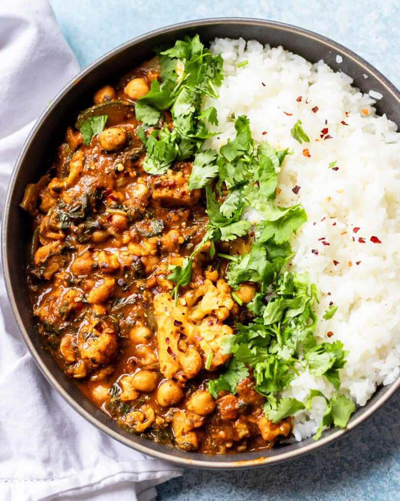 close up view of spicy vegan cauliflower curry with chickpeas, spinach, zucchini, and more with rice and cilantro.