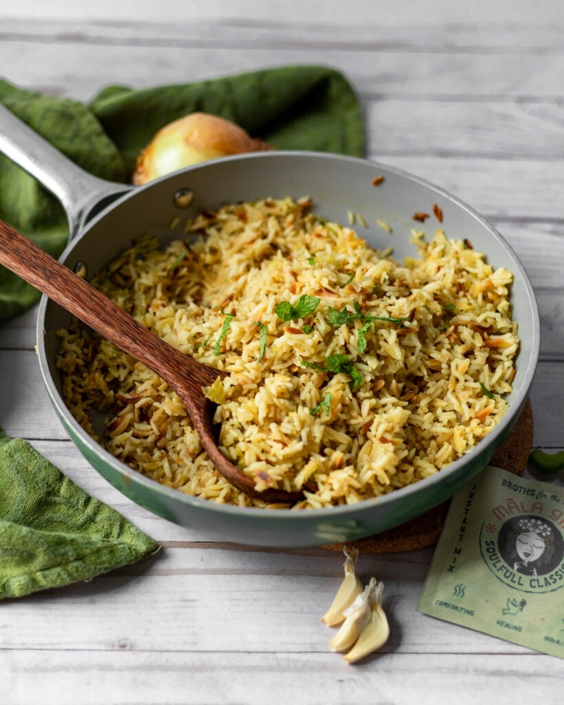 rice pilaf in a green pan with a spoon, with garlic and onions around it laid out flat