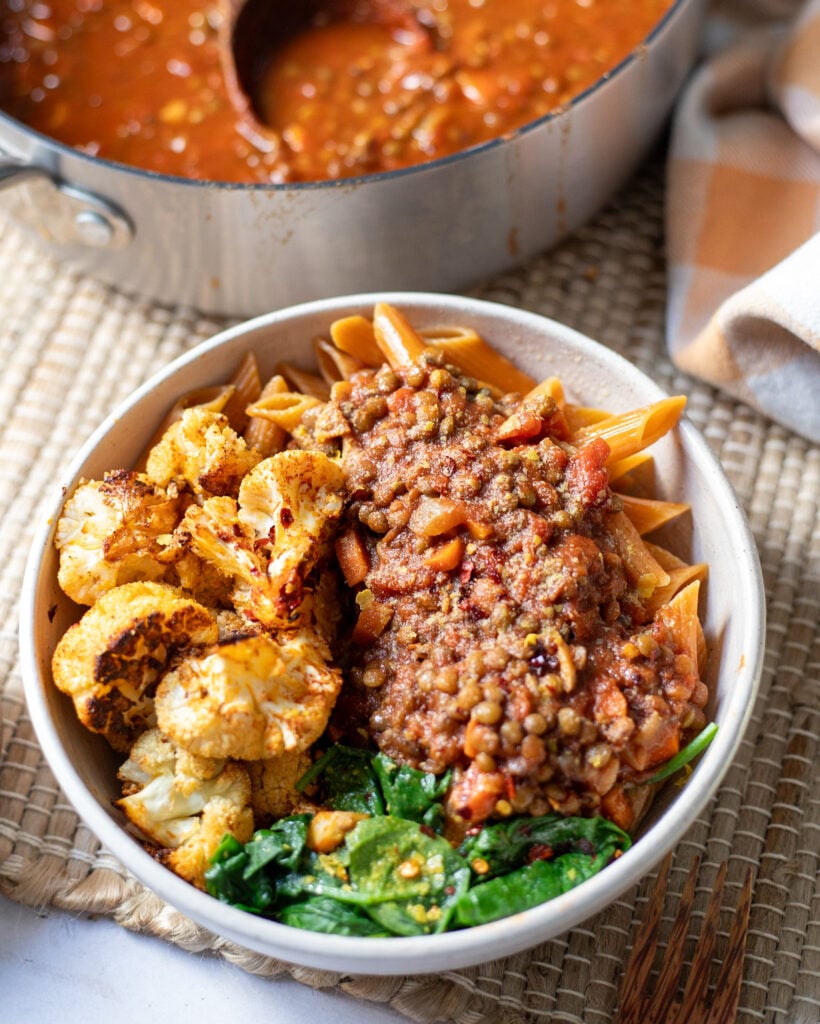 a serving dish with vegan green lentil bolognese next to a large saucepan with the pasta sauce ready to serve.