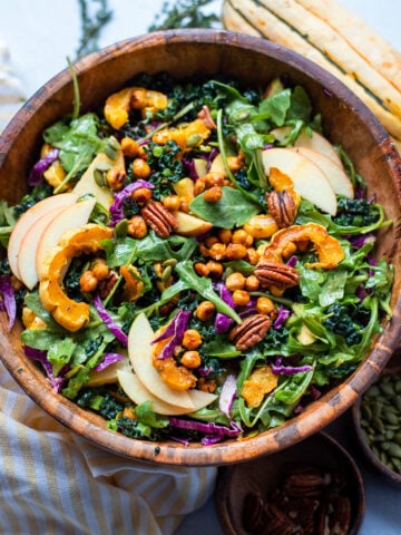 Overhead view of a large bowl filled with Fall Kale Salad topped with apples, delicata squash chickpeas and pecans