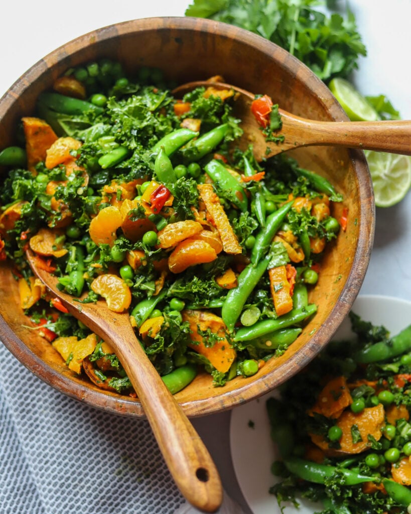 overhead view of a wooden bowl with a salad made with snow peas, mandarin oranges, kale, and more.