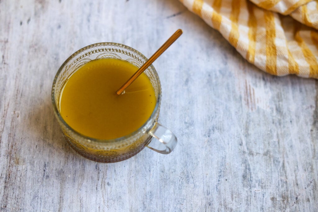 overhead view of a gray marble surface on which sits a glass bowl of sweet cider salad dressing next to a yellow and white dish cloth.