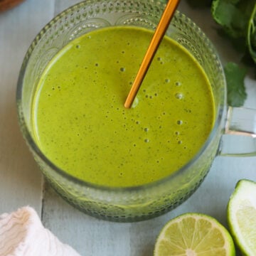 Glass serving dish of citrus mint salad dressing made with lemon and lime juice, olive oil, maple syrup, and fresh mint leaves on a table next to slices of fresh lemon