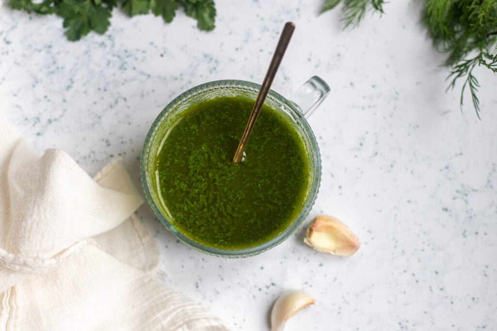 close up overhead view of a round salad dressing bowl of dark green garlic-herb dressing made with fresh parsley, dill, lemon juice, olive oil and garlic.