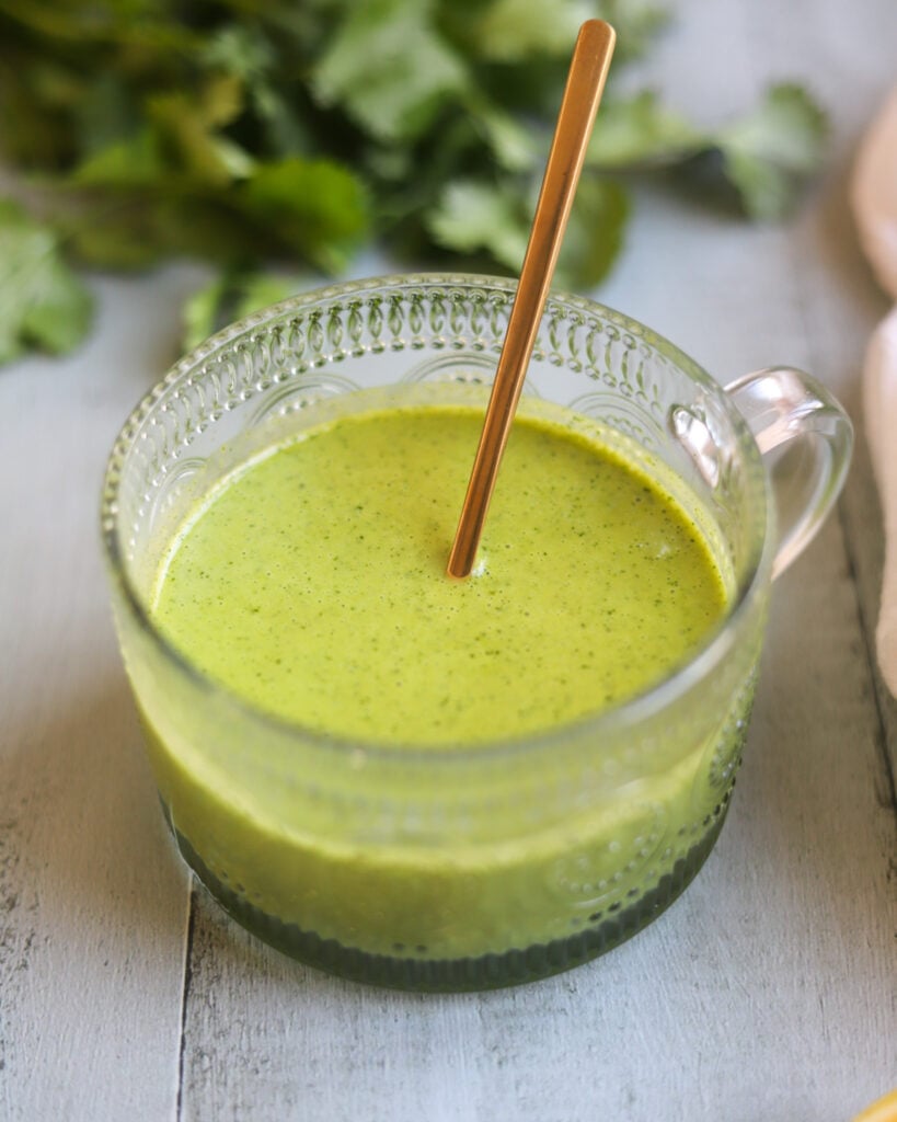 close up side view of a glass serving dish of fresh green sweet citrus salad dressing with fresh mint, maple syrup and olive oil along with lime and lemon juice.