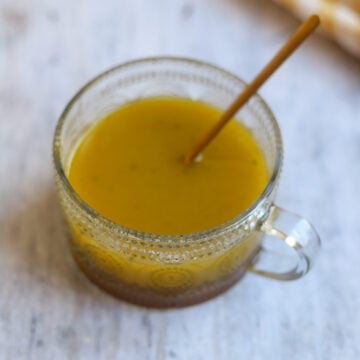 overhead view of round glass serving dish of maple cider vinegar dressing on a gray marble surface