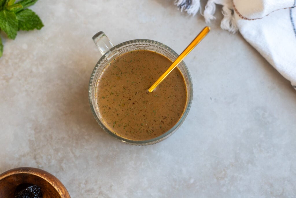 overhead view of a glass bowl of balsamic vinegar dressing made  with prunes, and fresh mint leaves.
