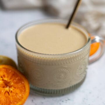 Round glass serving dish of orange tahini salad dressing made with maple syrup, sesame tahini, lemon and orange juice and salt. The dish is next to a mandarin orange slice on a table