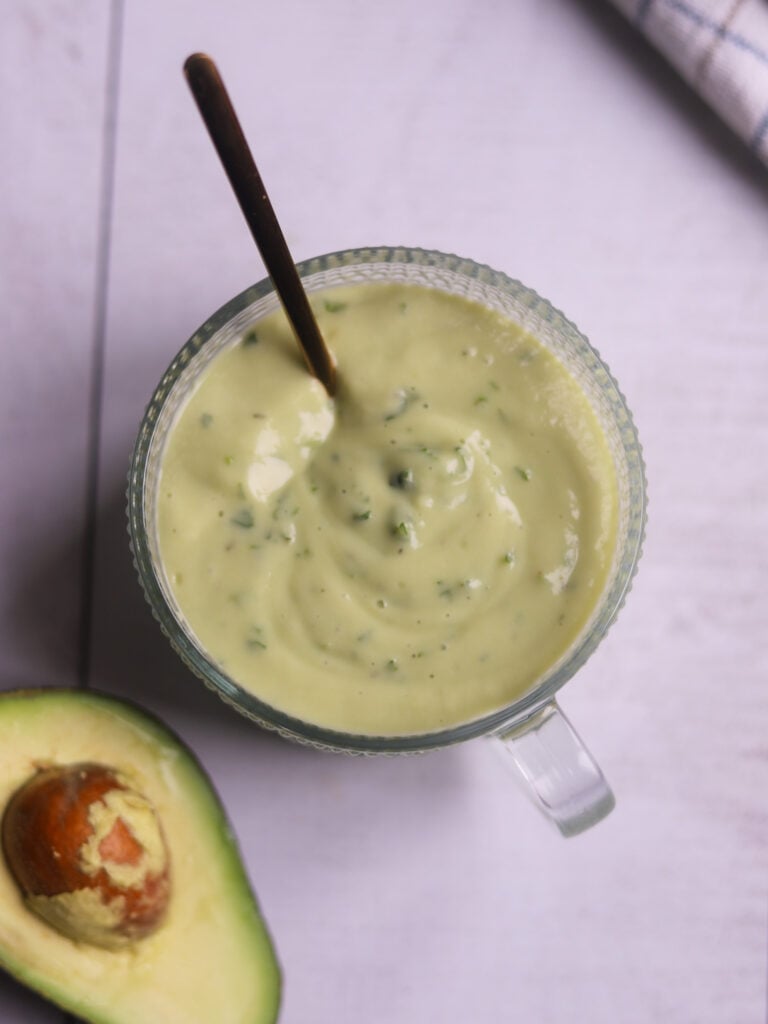 closuep overhead view of a bowl of ranch style avocado dressing next to a cut avocado half on a gray surface