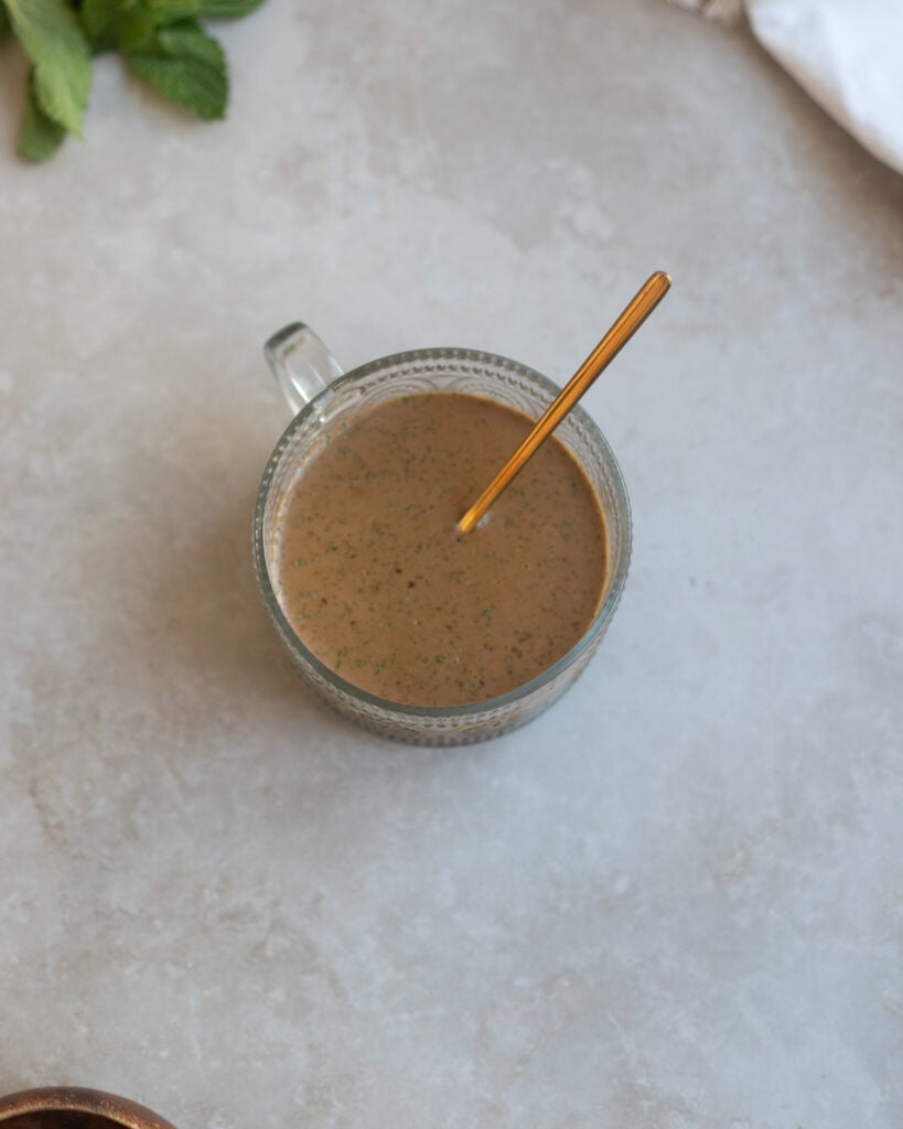 overhead view of fresh mint leaves along with a serving dish of prune mint balsamic salad dressing made with olive oil, fresh mint leaves, dried prunes, balsamic vinegar and salt.