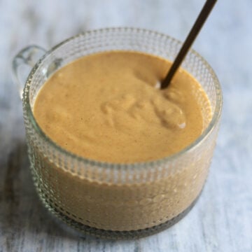 A glass bowl of peanut lime salad dressing made with soy sauce, sweet chili sauce, and rice vinegar along with smooth peanut butter, sits on a gray background