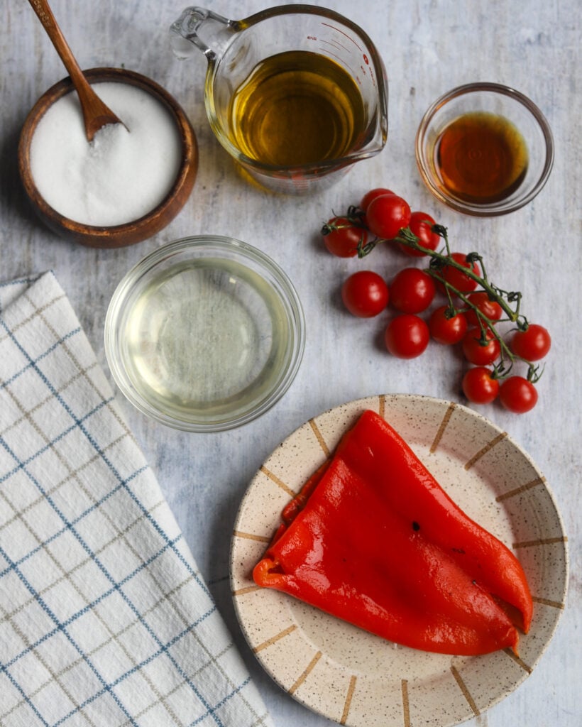 overhead view of all the ingredients to make roasted tomato and red pepper vinaigrette, like peppers, cherry tomatoes, balsamic vinegar, maple syrup, salt, and olive oil.