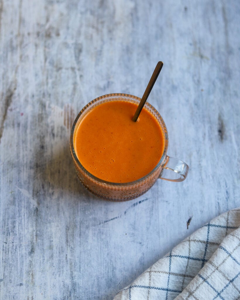 overhead view of a glass cup with a reddish orange roasted red pepper and tomato salad dressing.