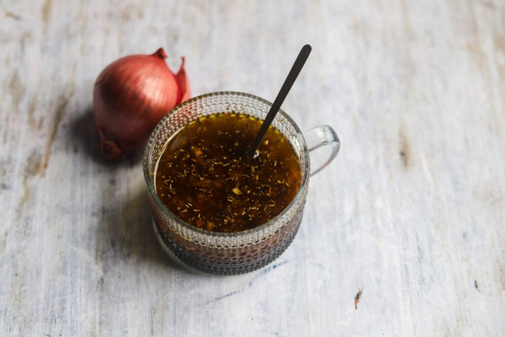 side view of a glass cup with homemade sweet red onion salad dressing in front of a red onion.
