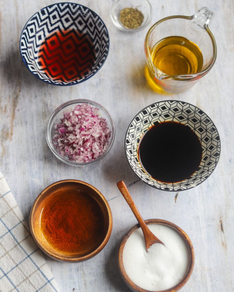 overhead view of the ingredients to make red onion vinaigrette, like vinegar, oil, dried herbs, and finely minced red onion.
