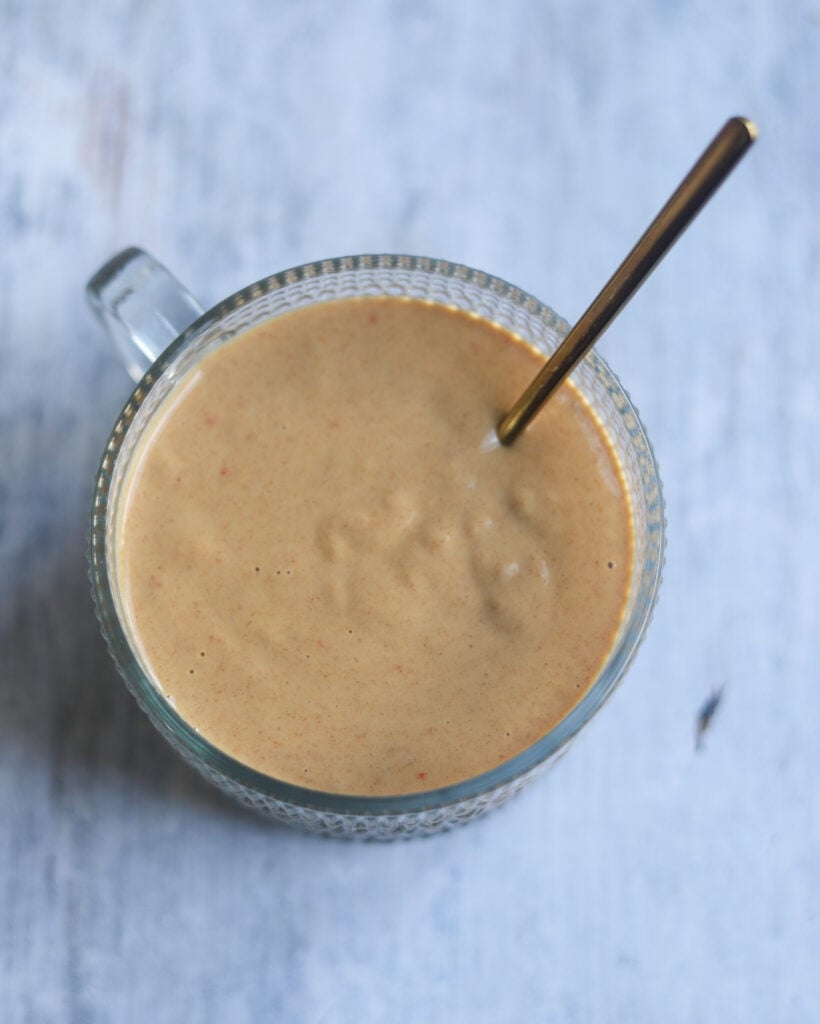 closeup overhead view of a bowl of creamy tan tangy lime peanut dressing that includes sweet chili sauce, fresh lime juice, soy sauce and unsalted peanut butter sits on a gray surface.