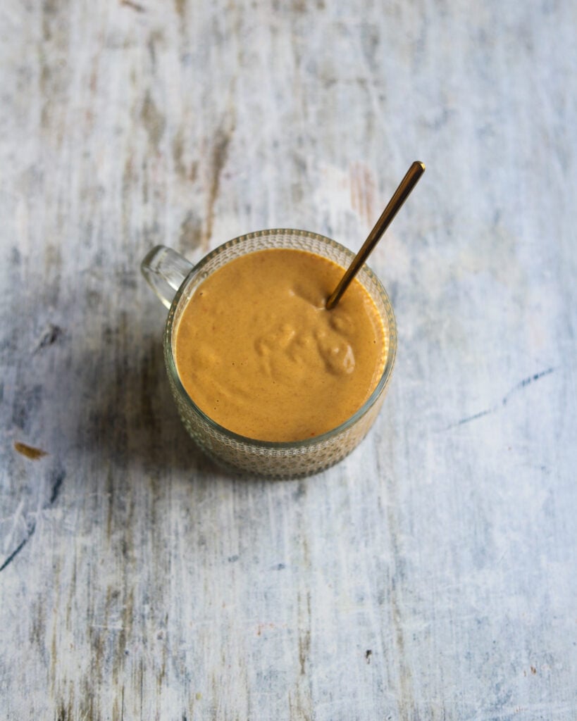 overhead view of a round glass dish containing vegan lime peanut salad dressing made with rice vinegar, fresh lime juice, sweet chili sauce, soy sauce and smooth peanut butter sits on a gray marble background.