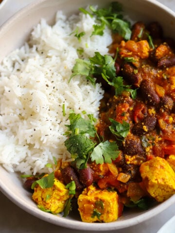 Overhead view of a bowl filled half with rice and half with Rajma curried kidney beans and tofu in a tomato and curry sauce with cilantro garnish.