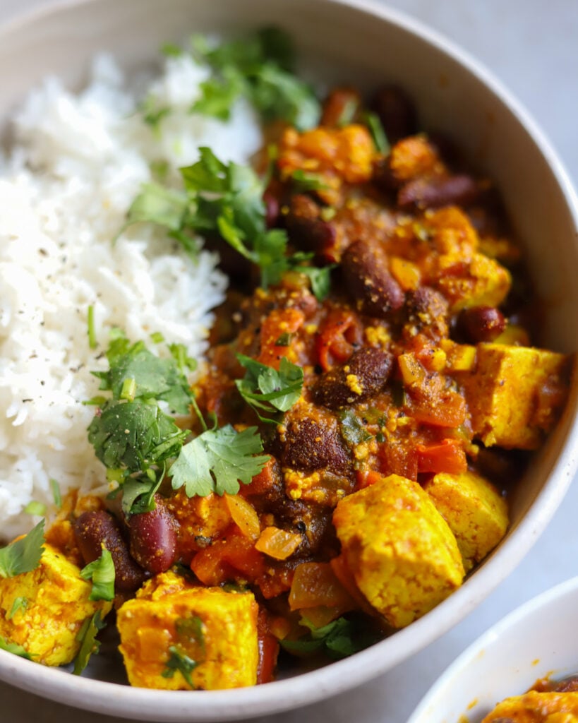 Closeup of a bowl of curry rajma kidney beans with tofu in a tomato and curry sauce with rice and a sprinkle of cilantro