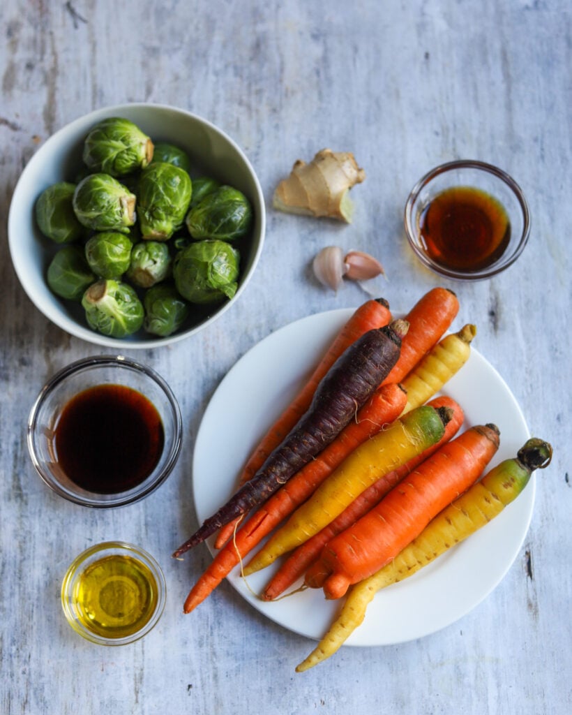 Ingredients for maple brussels sprouts laid out flat before cooking. Carrots, brussels, ginger, garlic, soy sauce, maple syrup, extra virgin olive oil