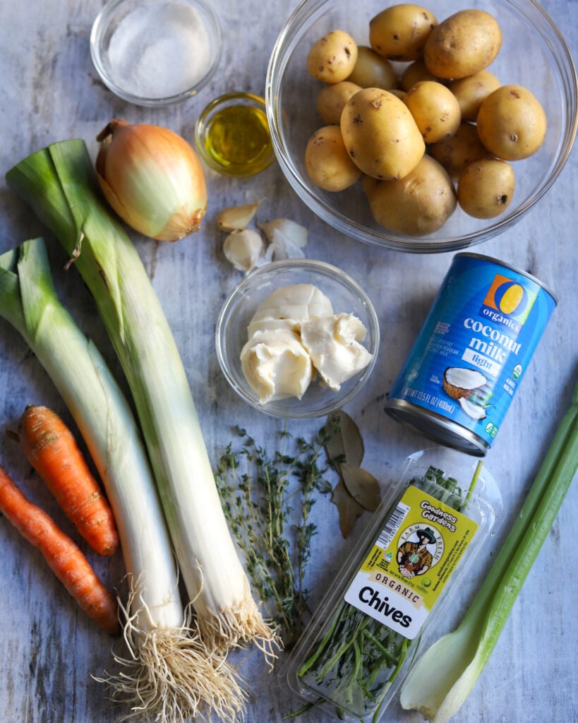 ingredients for potato leek soup laid out flat, potatoes, leeks, butter, garlic, celery, carrots, chives, thyme. coconut milk and olive oil