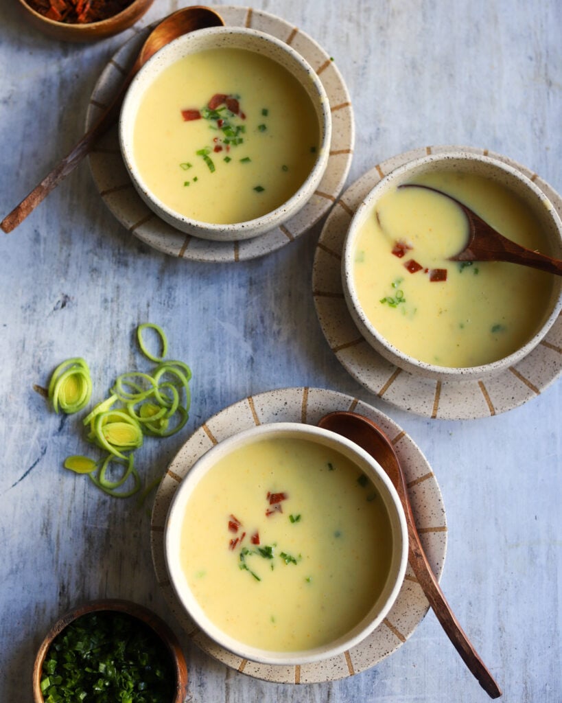 overhead view of 3 bowls of potato leek soup with some chopped leeks on the table on the side