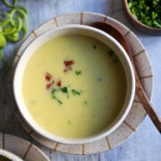 Overhead view of a bowl of creamy potato leek soup with chives and bacon bits for garnish