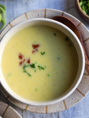 Overhead view of a bowl of creamy potato leek soup with chives and bacon bits for garnish