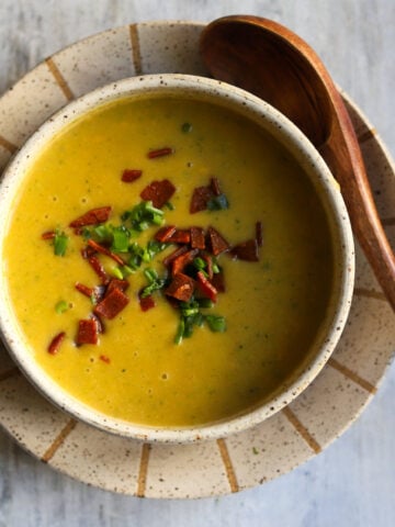 overhead view of cheddar broccoli soup with bacon and chives on top with a spoon on the side