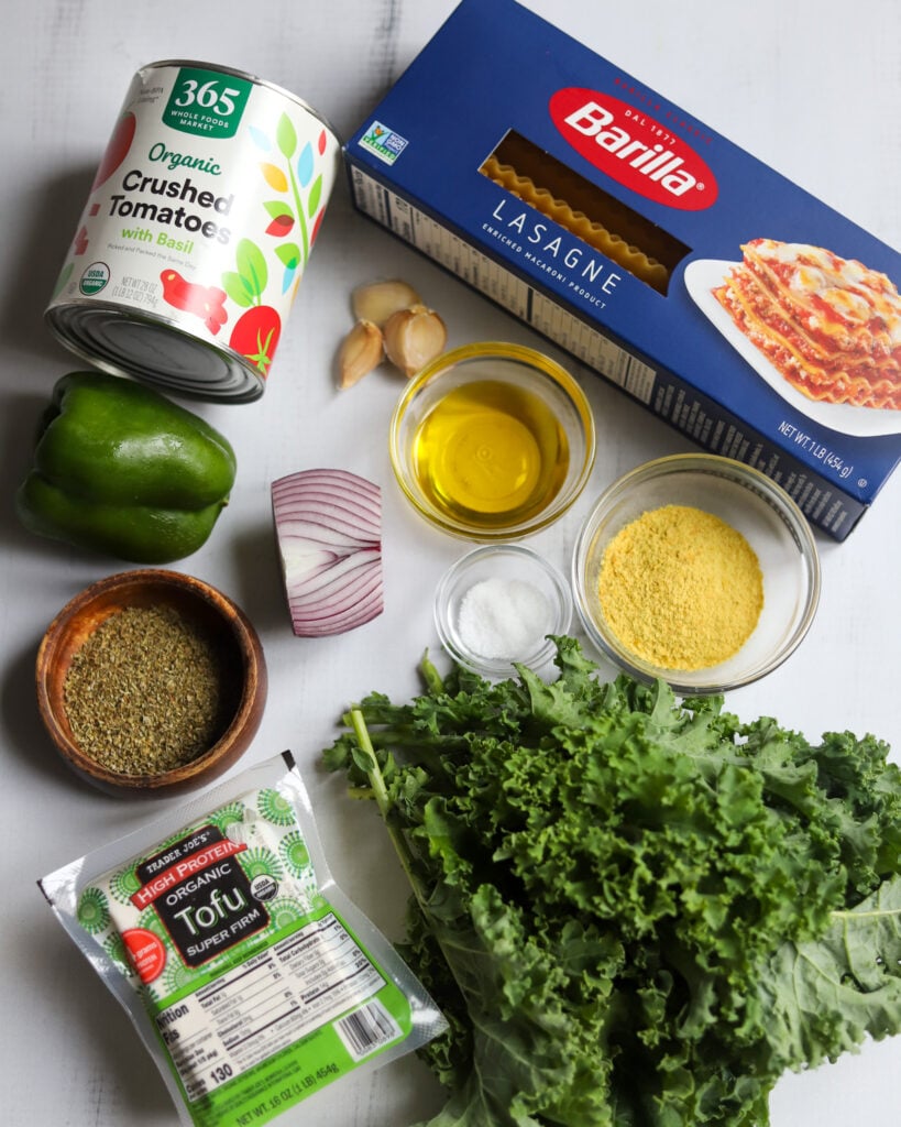 Ingredients for Lasagna Soup in a flatlay arrangement, crushed tomatoes, lasagna noodles, firm tofu, olive oil, onion and garlic, green pepper, kale and spices