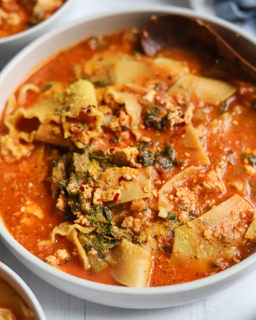 closeup of a large bowl of soup filled with noodles, tomato sauce, greens and nutritional yeast sprinkled on top