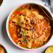 Overhead shot looking into a large bowl of soup with noodles, tomato sauce, greens and nutritional yeast