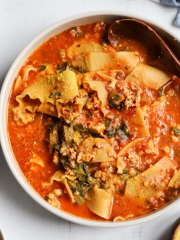 Overhead shot looking into a large bowl of soup with noodles, tomato sauce, greens and nutritional yeast
