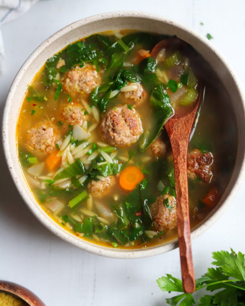 Closeup of a bowl of Italian wedding soup with meatballs, greens and carrots