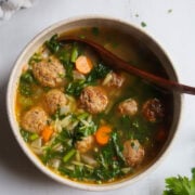 overhead view of a bowl of Italian Wedding Soup with a spoon in it and 8 mini meatballs