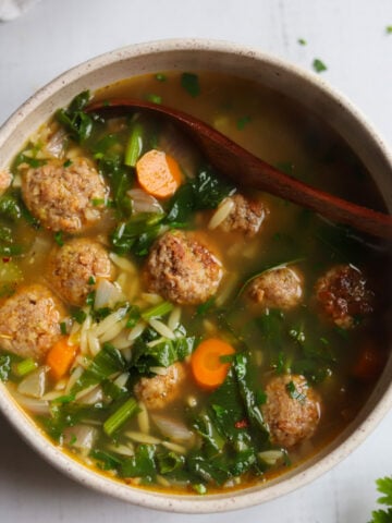 overhead view of a bowl of Italian Wedding Soup with a spoon in it and 8 mini meatballs