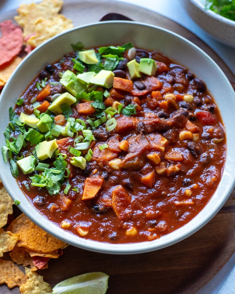 close up view of a bowl of black bean and sweet potato chili topped with avocado and cilantro