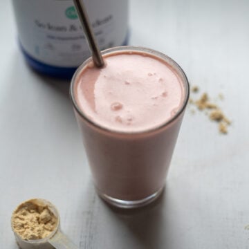 45 degree angle looking into a glass full of pink strawberries and cream smoothie