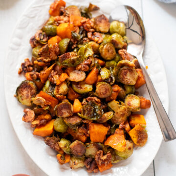 Overhead view of a white platter with roasted brussels sprouts and squash with walnuts