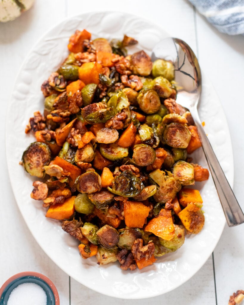 Overhead view of a white platter with roasted brussels sprouts and squash with walnuts