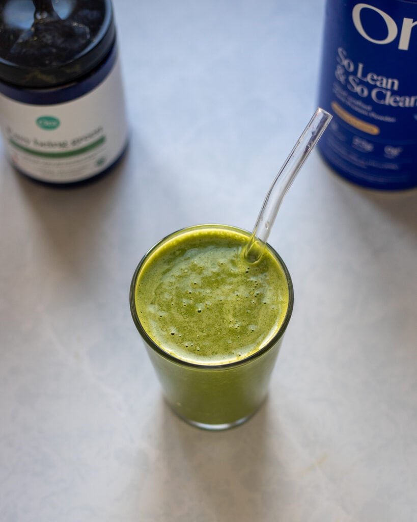overhead view of healthy green smoothie with vegan protein powder with the jug of protein powder and the greens powder in the background