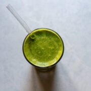 Overhead view of healthy green smoothie with vegan protein powder in a glass with a straw