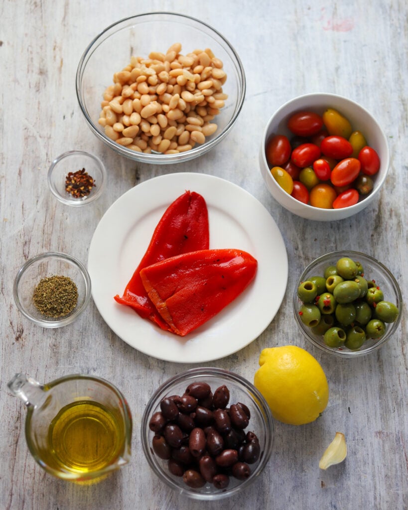 overhead view of ingredients for marinated olive salad with beans laid out in bowls in a flatlay