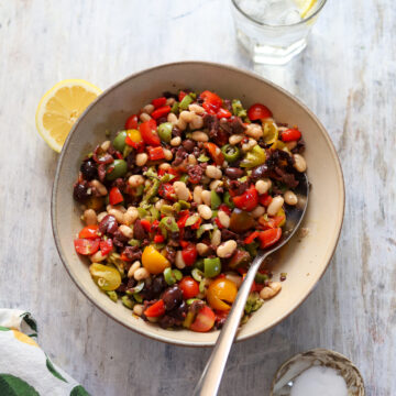 overhead view looking into a large bowl of marinated olive salad with beans, tomatoes and peppers.