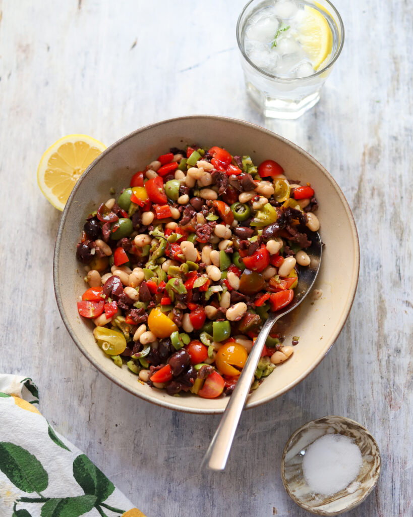 overhead view looking into a large bowl of marinated olive salad with beans, tomatoes and peppers.