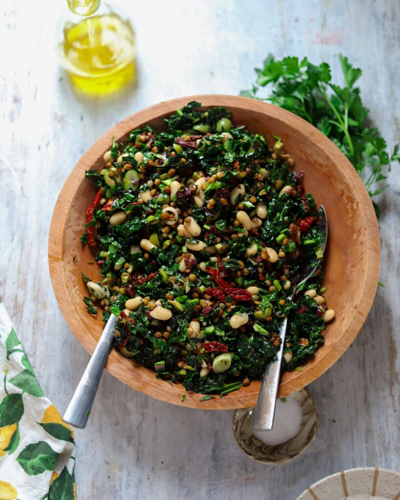 overhead view of a kale salad with lentils, beans, olives and sun-dried tomatoes in a wood bowl